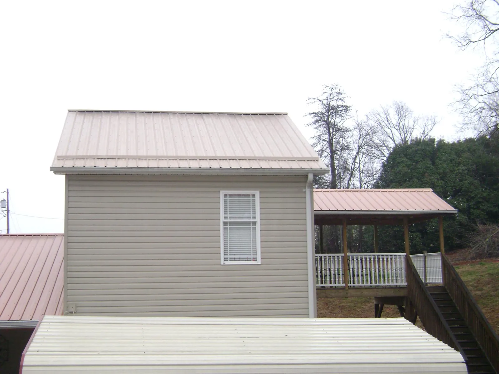 Tan metal roofs on a two story addition and attached porch, from a Roof Replacement job in Concord